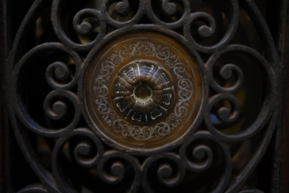 Close-up of ornate wrought iron scrollwork around a round brass medallion on a dark Venetian door