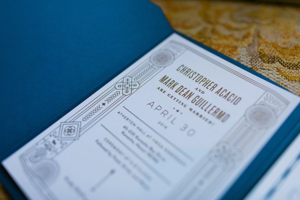 Close-up of a letterpress-style wedding invitation with Art Deco borders announcing an April 30 ceremony