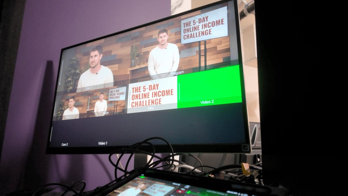 Multicam switcher monitor showing camera angles of a host on the wood-wall set and a title card reading The 5-Day Online Income Challenge, at a studio in San Diego