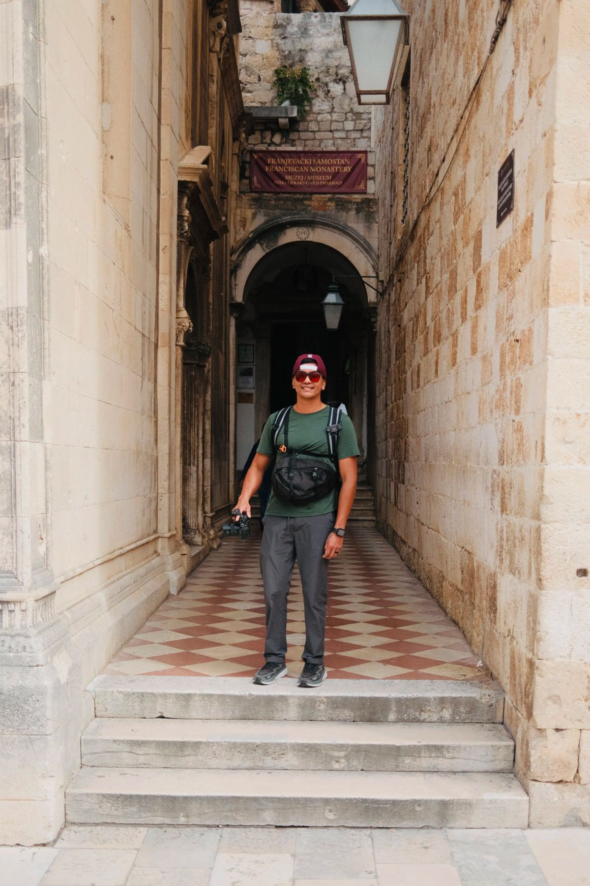 A man in a cap stands in a stone passage leading to a sign for the Franciscan Monastery