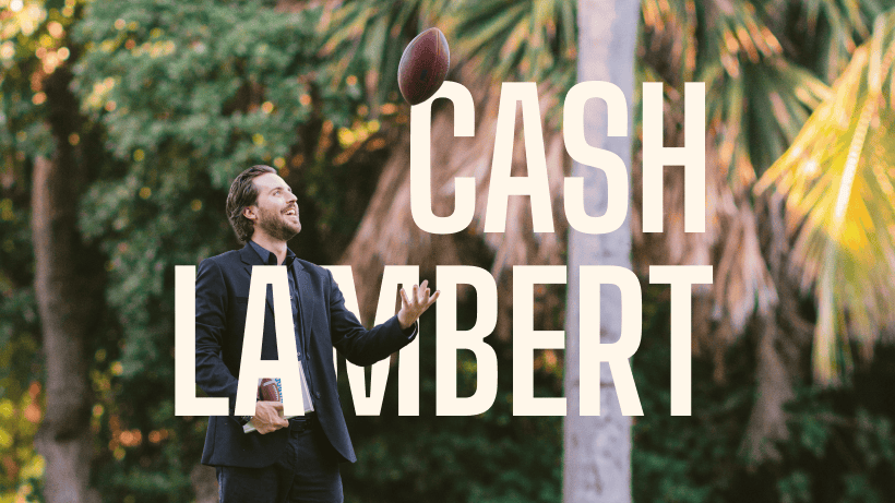 Cash Lambert in a dark suit on a lawn under palm trees, holding a copy of Changing the Playbook and tossing a football in the air.