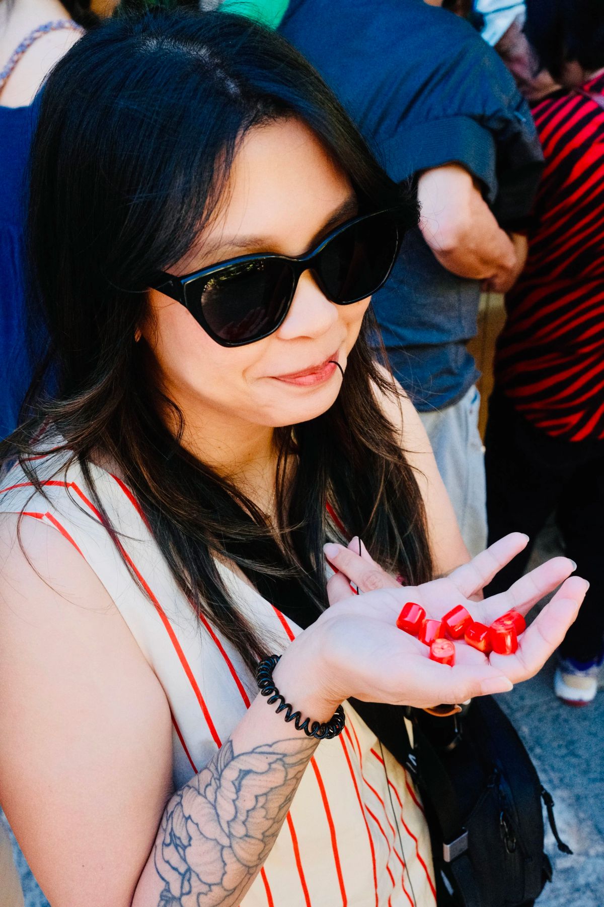 A woman in sunglasses smiles while holding a handful of red beads for her komboloi