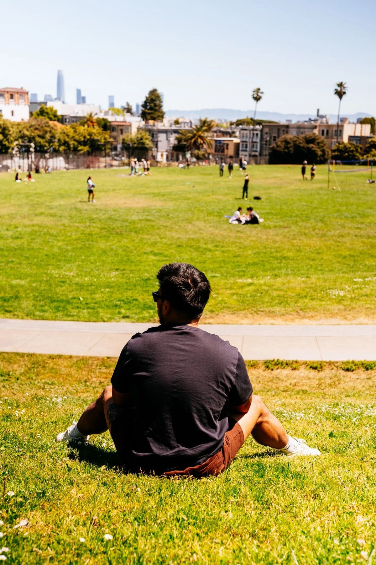 Man sitting on the grass at Dolores Park with the San Francisco skyline in the distance