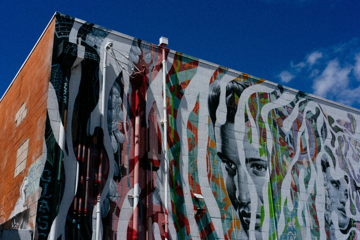 Large mural of flowing multicolored lines and a painted face spread across a brick building wall