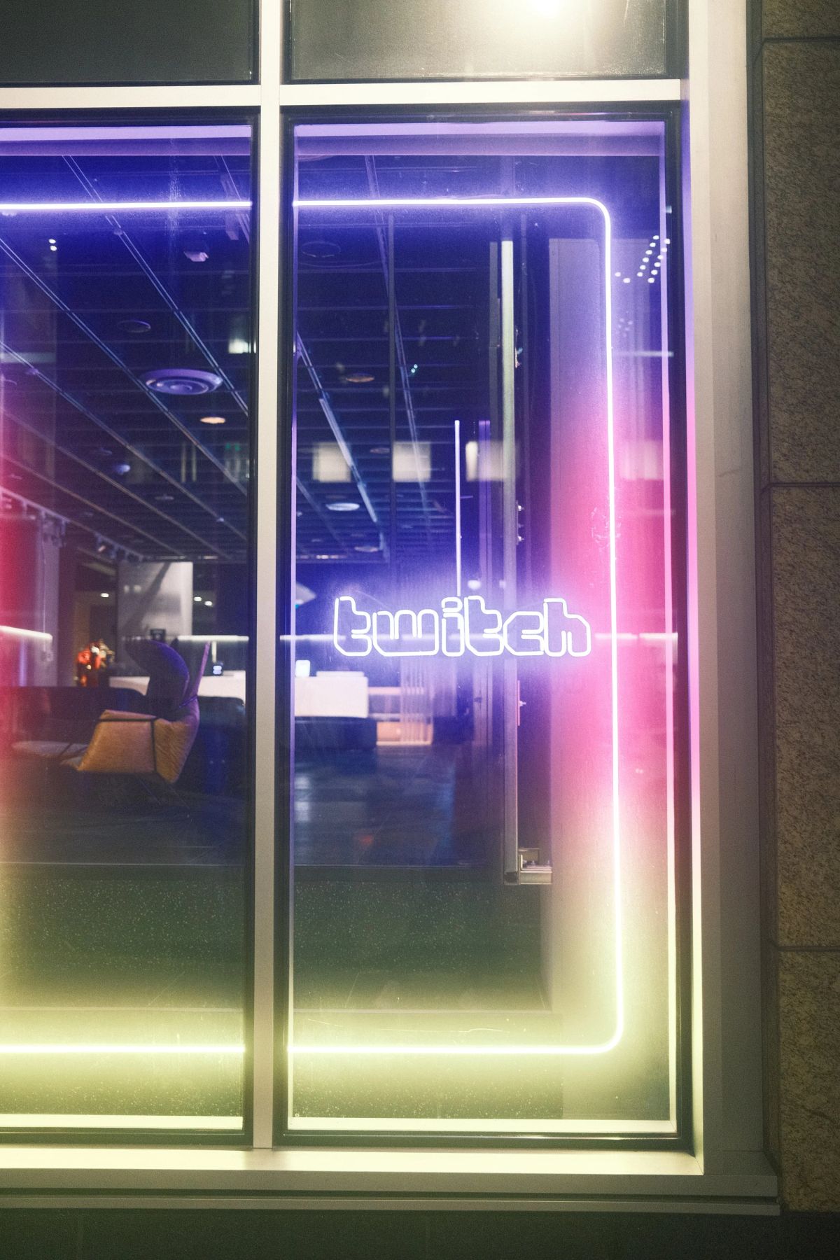 Street view of the Twitch office window at night, its neon wordmark and gradient light frame glowing