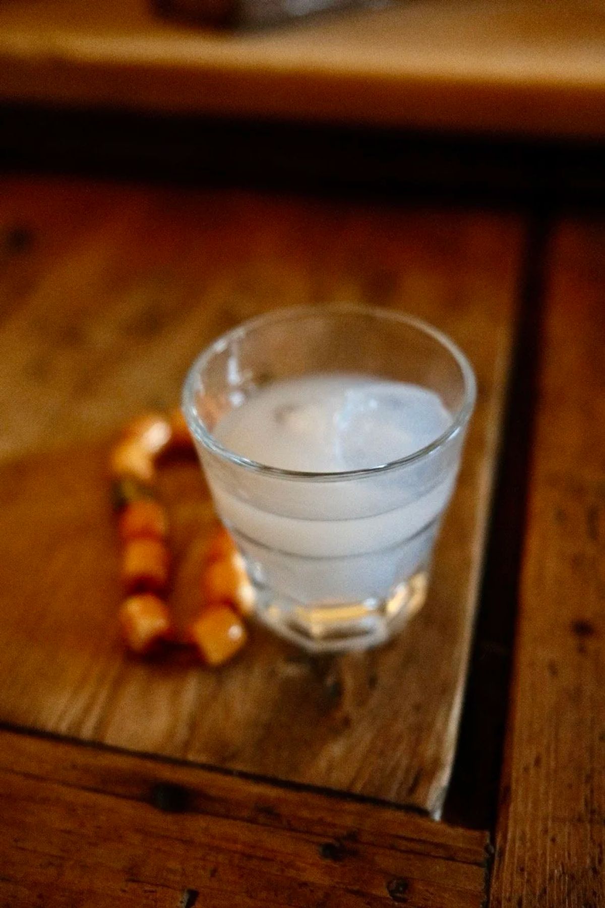 A glass of cloudy ouzo with ice on a wooden table beside an orange beaded komboloi