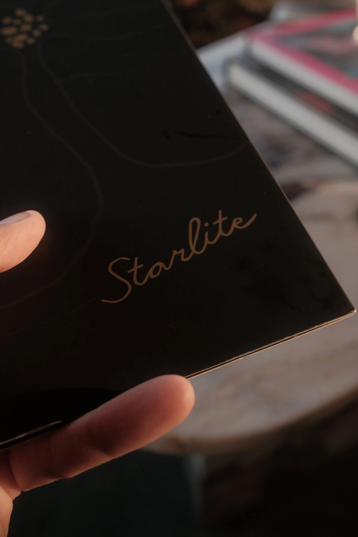 A hand holds a black menu with gold "Starlite" script lettering in warm evening light