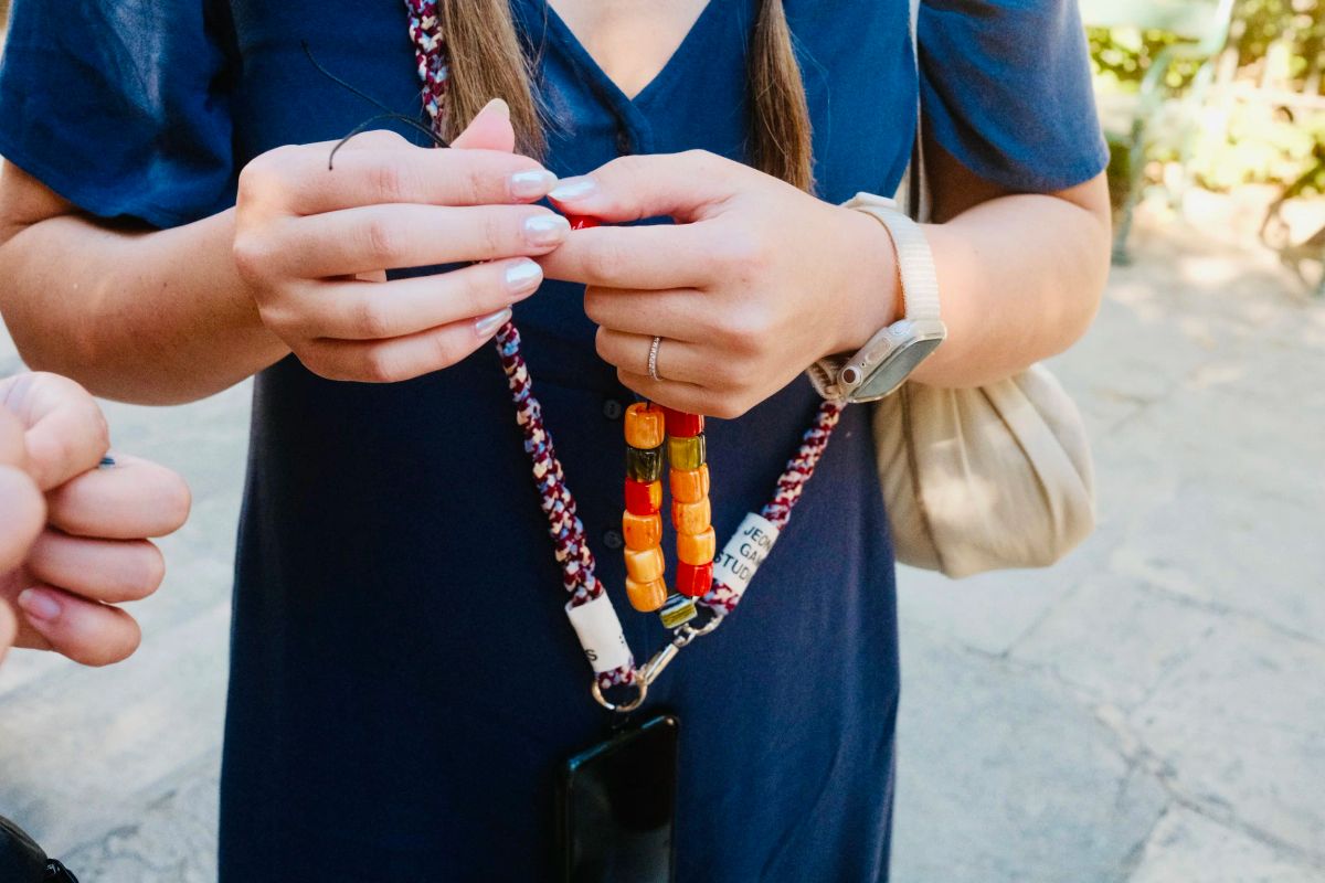 Close-up of hands holding a handmade komboloi of orange and red beads on a braided lanyard