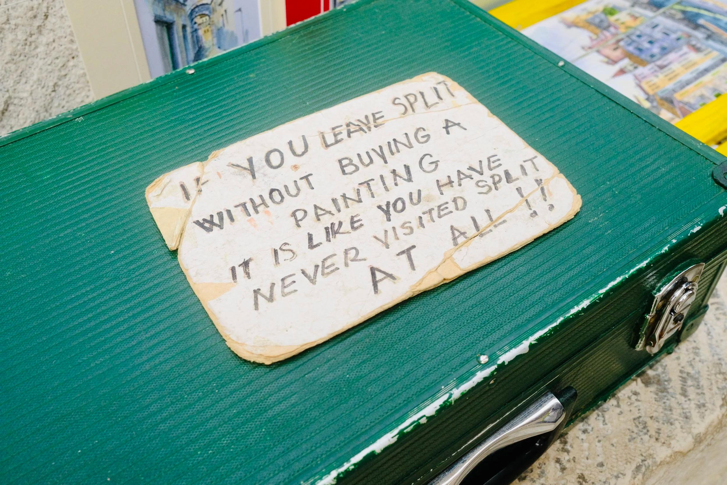 Handwritten sign in Split saying leaving without buying a painting is like never visiting