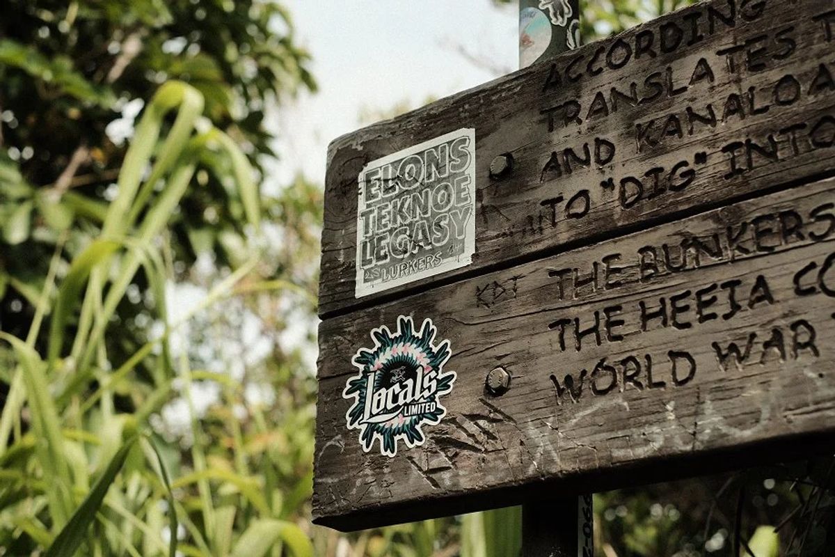 Weathered carved wooden trail sign describing the Heeia World War II bunkers, covered in stickers