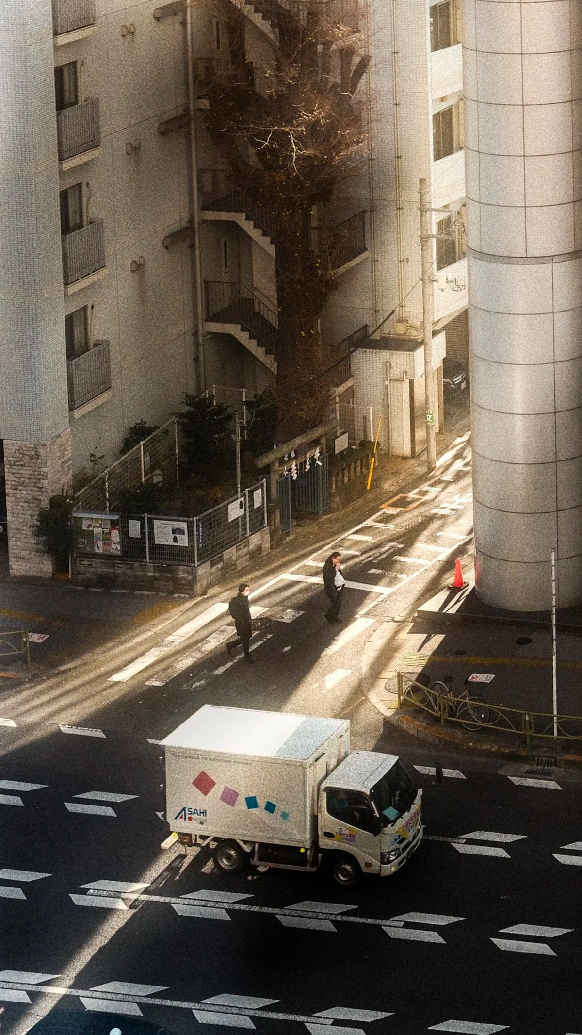 Elevated view of a Tokyo crosswalk in raking morning light as a delivery truck passes two pedestrians
