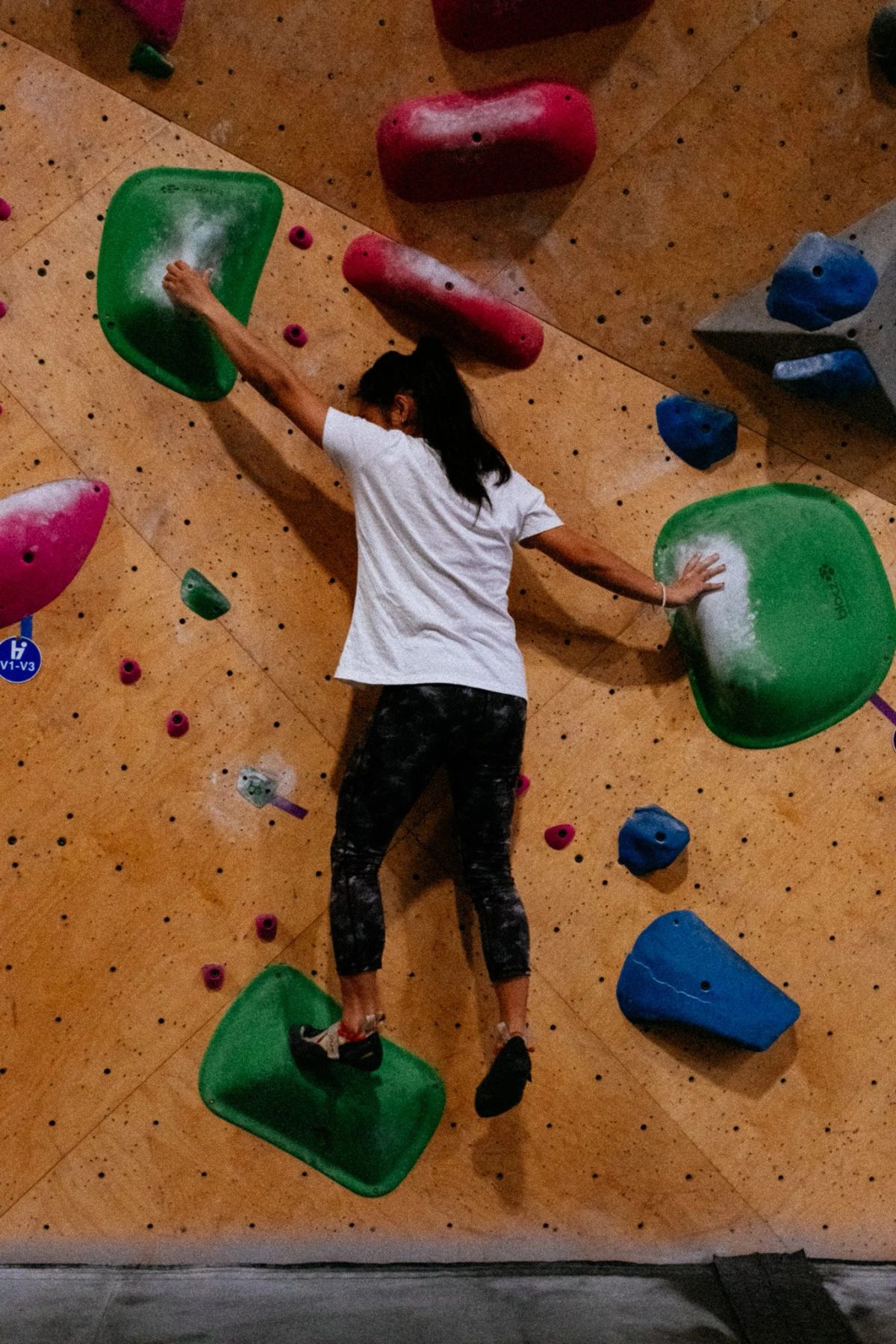 Climber in a white tee stretched between green holds on a bouldering wall