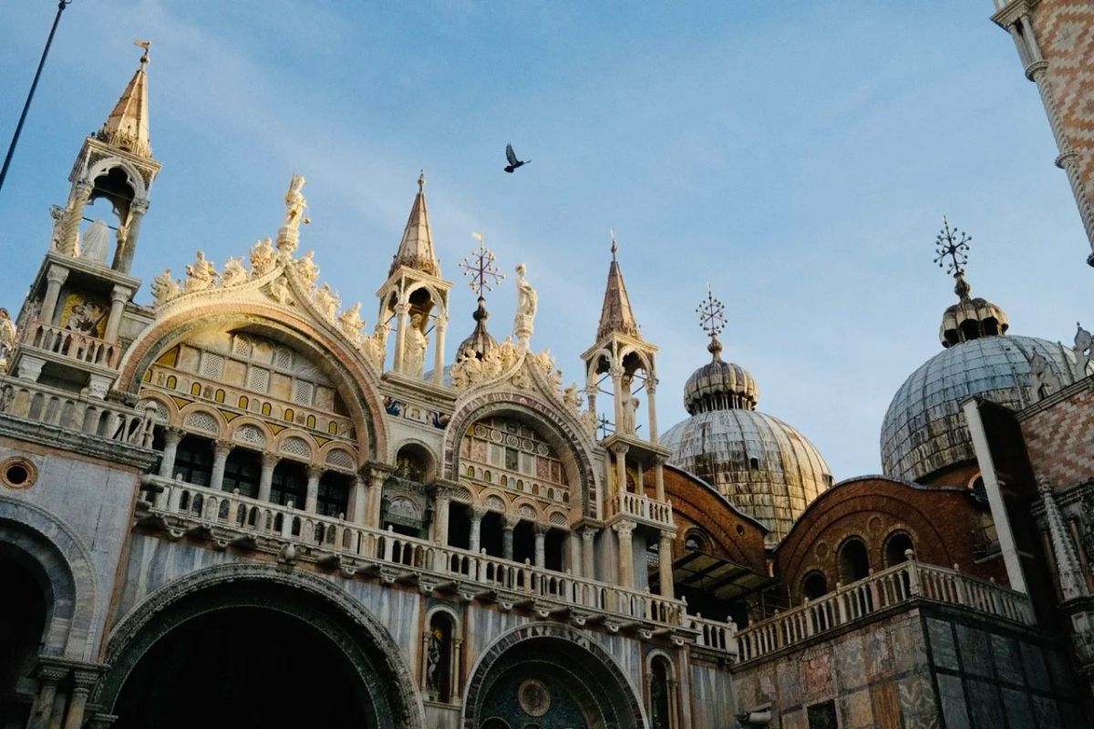 Gilded spires, arches and domes of St. Mark's Basilica in Venice against a blue sky with a bird