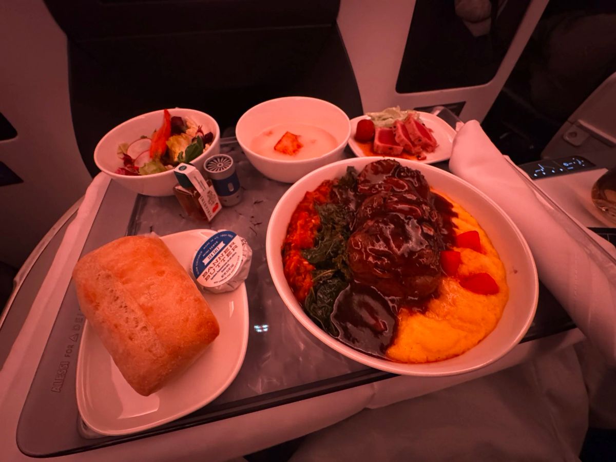 In-flight business class meal of braised meat over polenta with greens, plus a salad, bread roll and butter