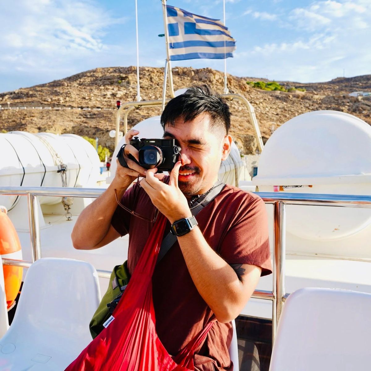A man photographing from a boat with a Greek flag flying behind him