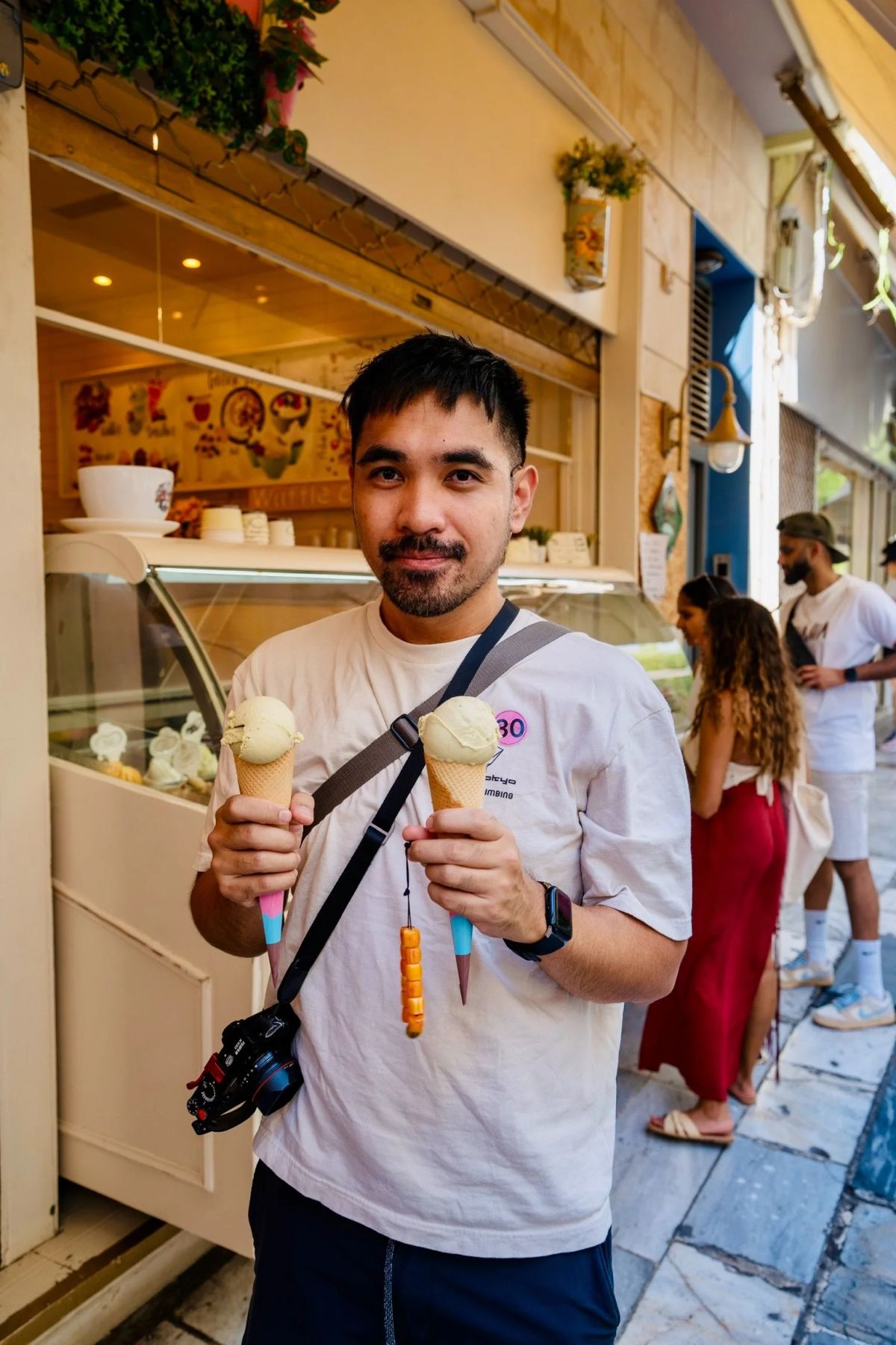 A man holding two gelato cones outside a gelato shop in Athens
