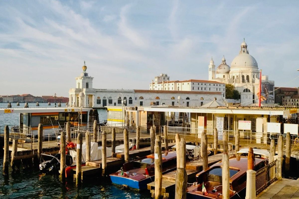 Wooden water taxis docked at pilings in Venice, with the white dome of Santa Maria della Salute behind