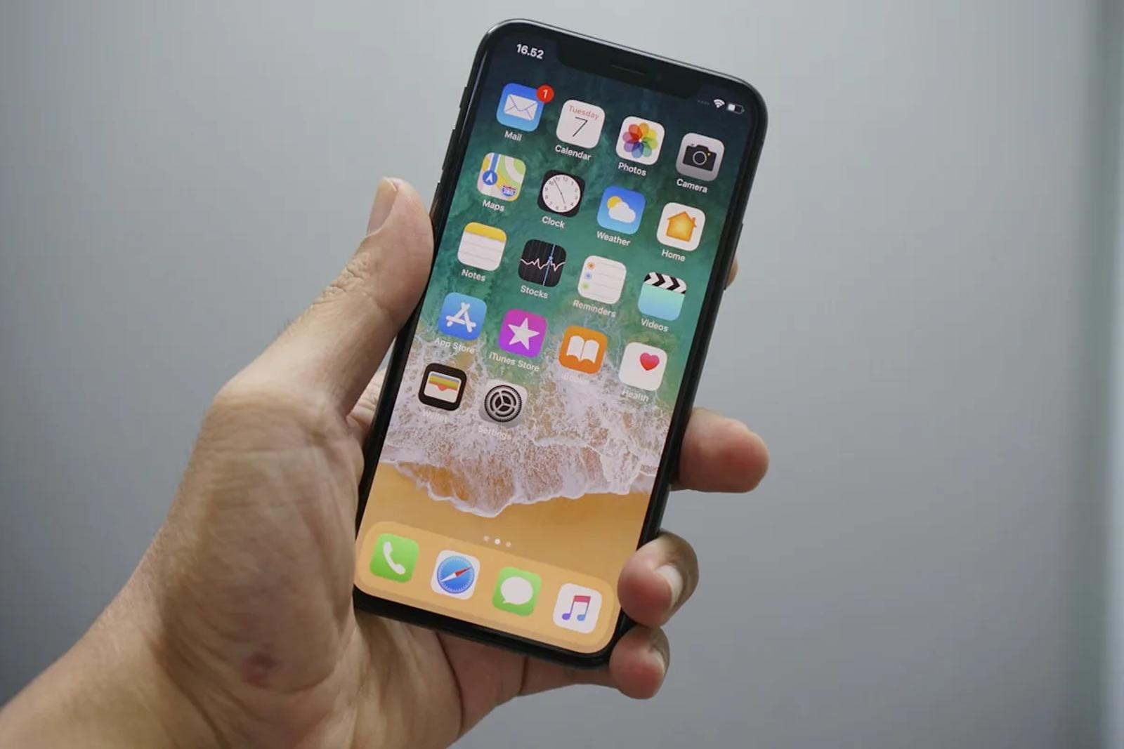 A hand holding an iPhone with the home screen open, ready to enter the Settings menu