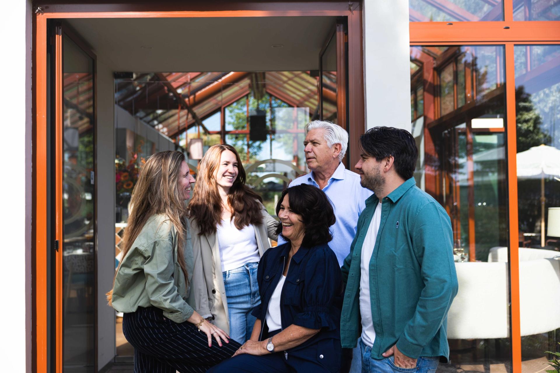 Familie Bergwerff lacht samen bij de glazen ingang van De Kas, de eventlocatie van La Cocotte in Hoogvliet.