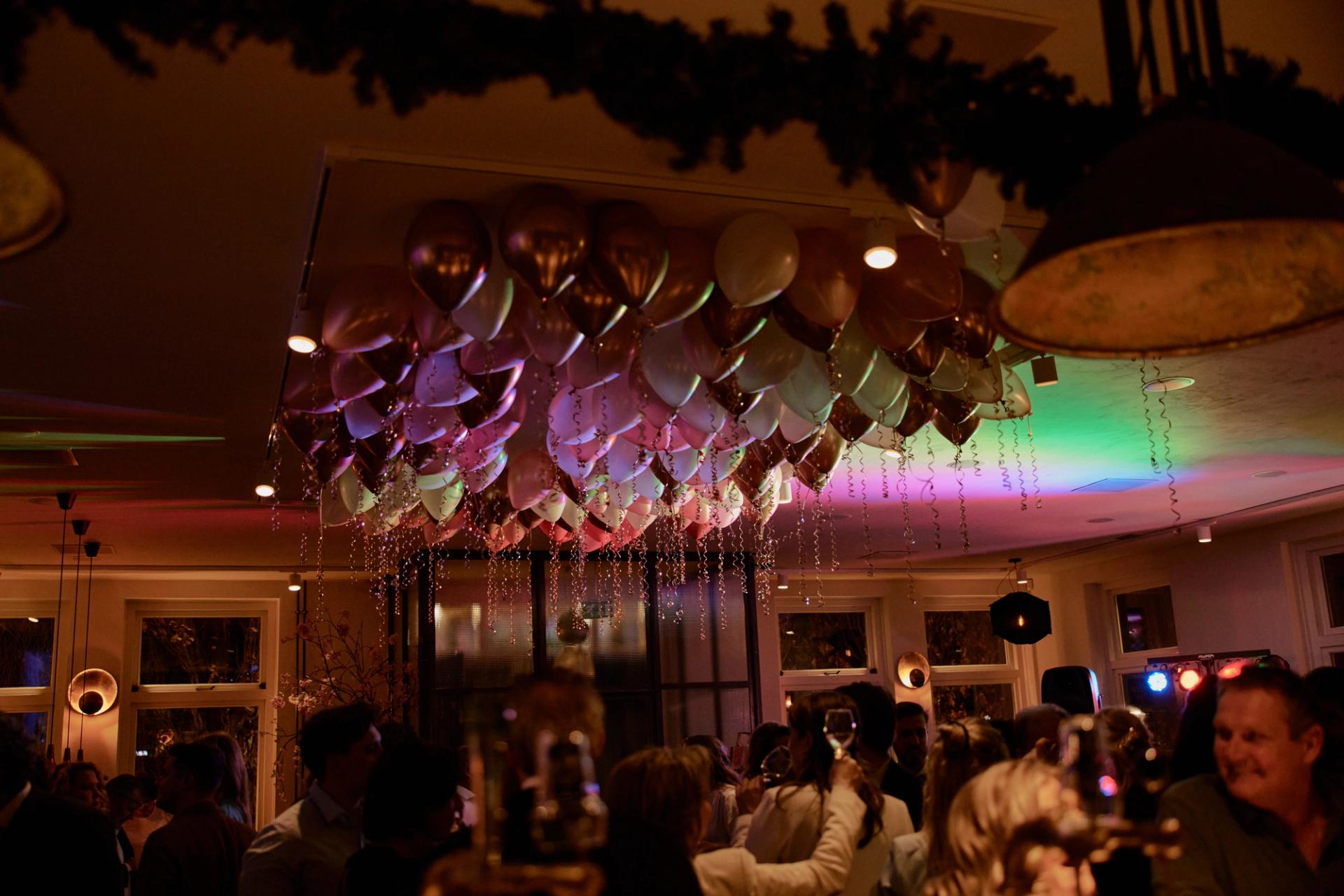 Bedrijfsfeest in het restaurant van La Cocotte, met een plafond vol ballonnen en gasten onder gekleurd feestlicht