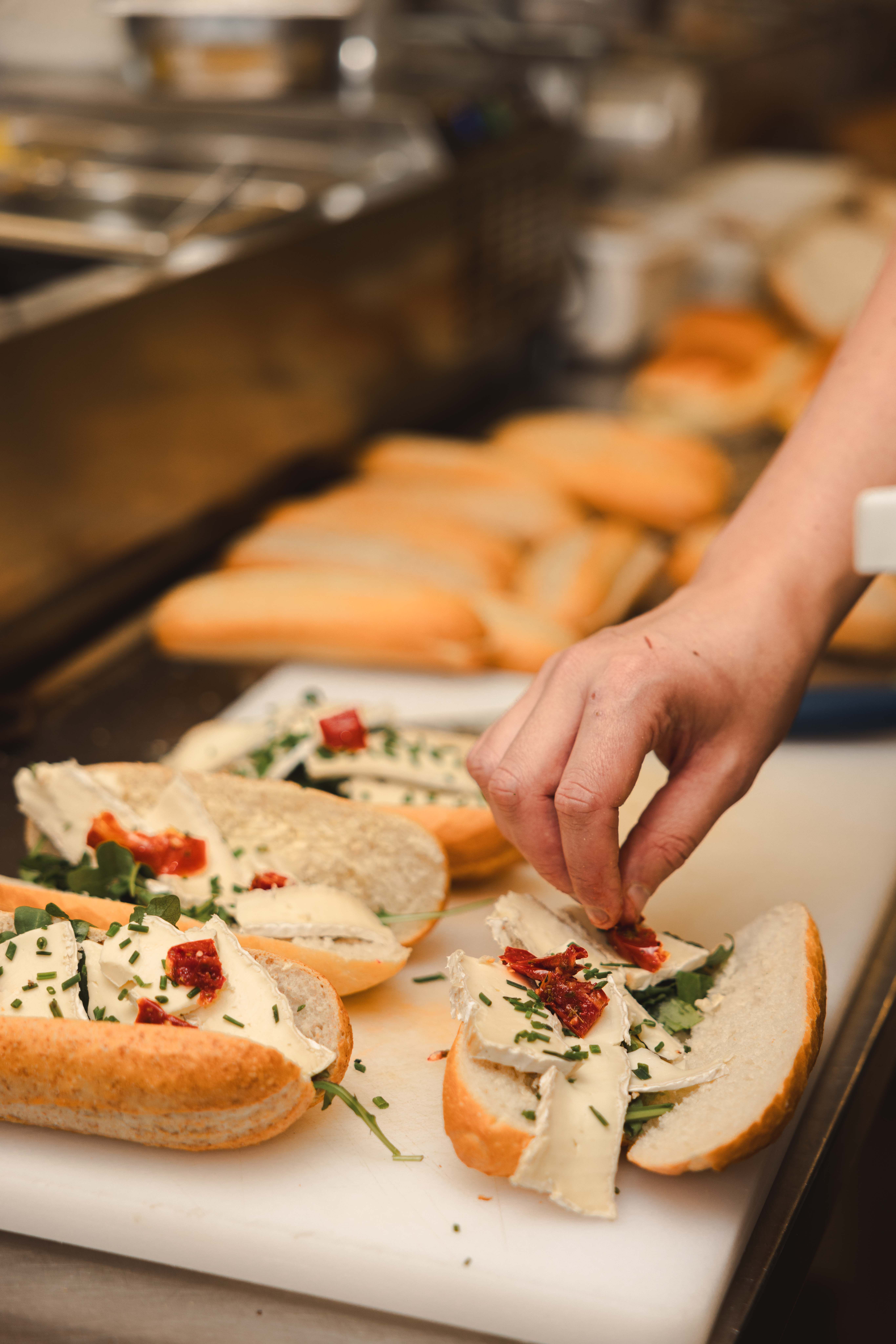 Kok belegt verse stokbroodjes met brie, zongedroogde tomaat, rucola en bieslook voor de lunchcatering van La Cocotte
