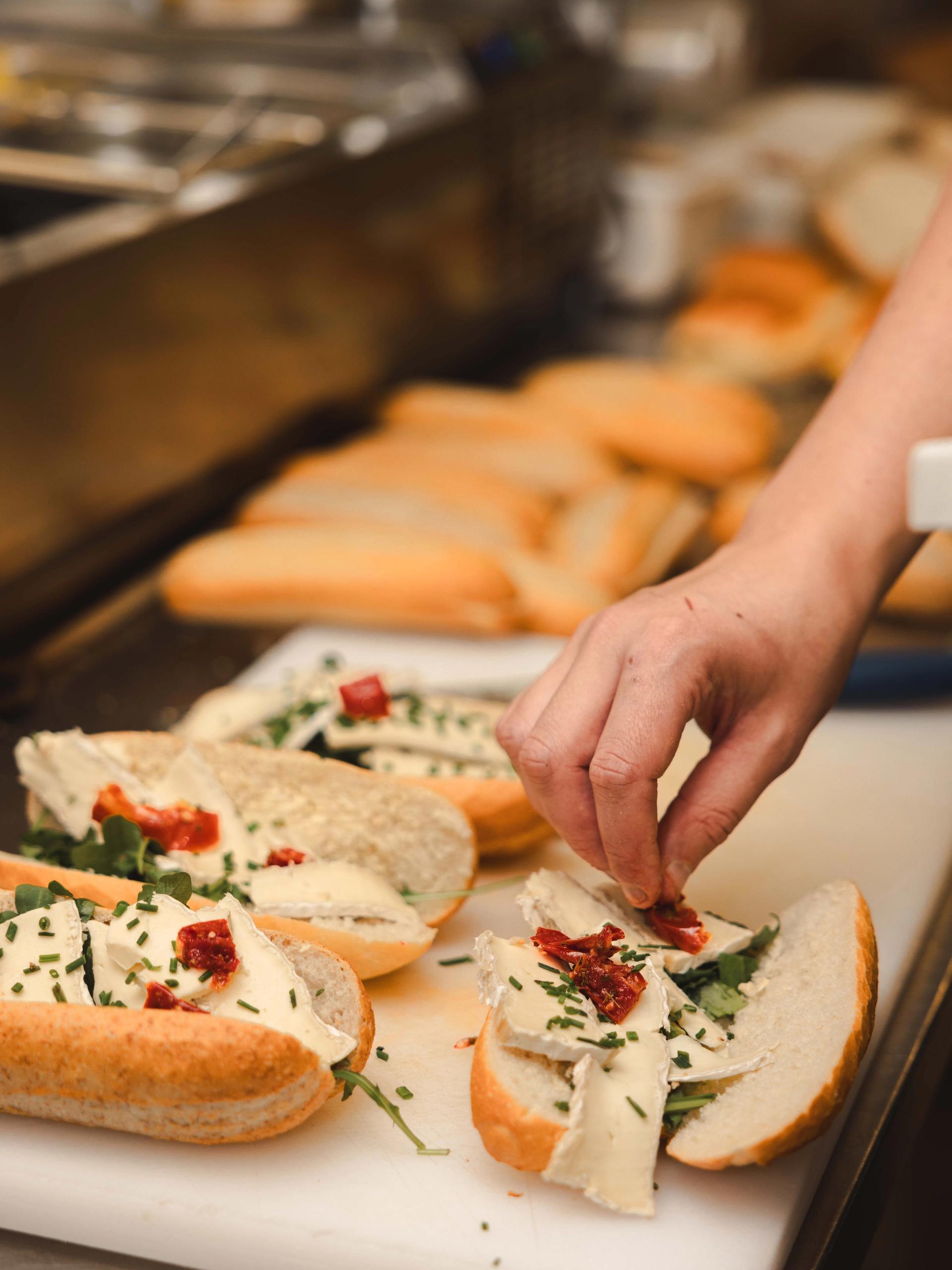 Kok belegt verse stokbroodjes met brie, zongedroogde tomaat, rucola en bieslook voor de lunchcatering van La Cocotte