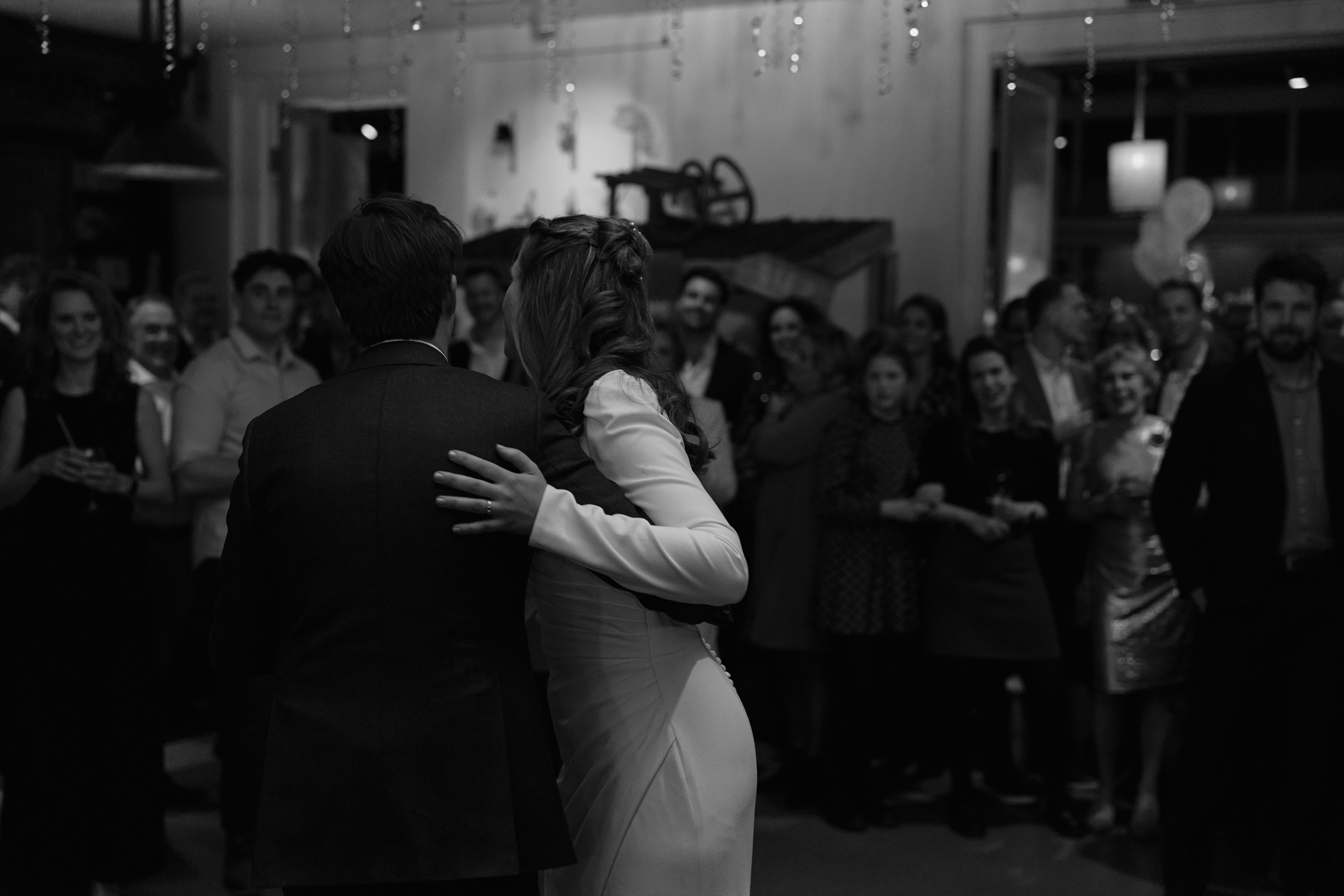 Zwart-witfoto van de openingsdans van het bruidspaar, omringd door gasten op het feest bij La Cocotte