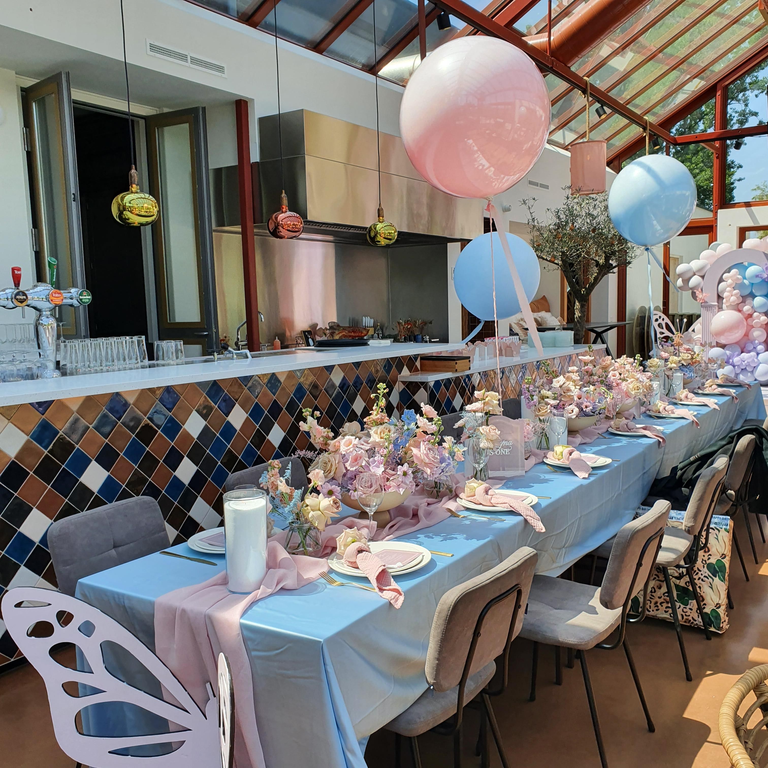 Babyshower in restaurant met roze en blauwe aankleding en versiering op gedekte lange tafels.