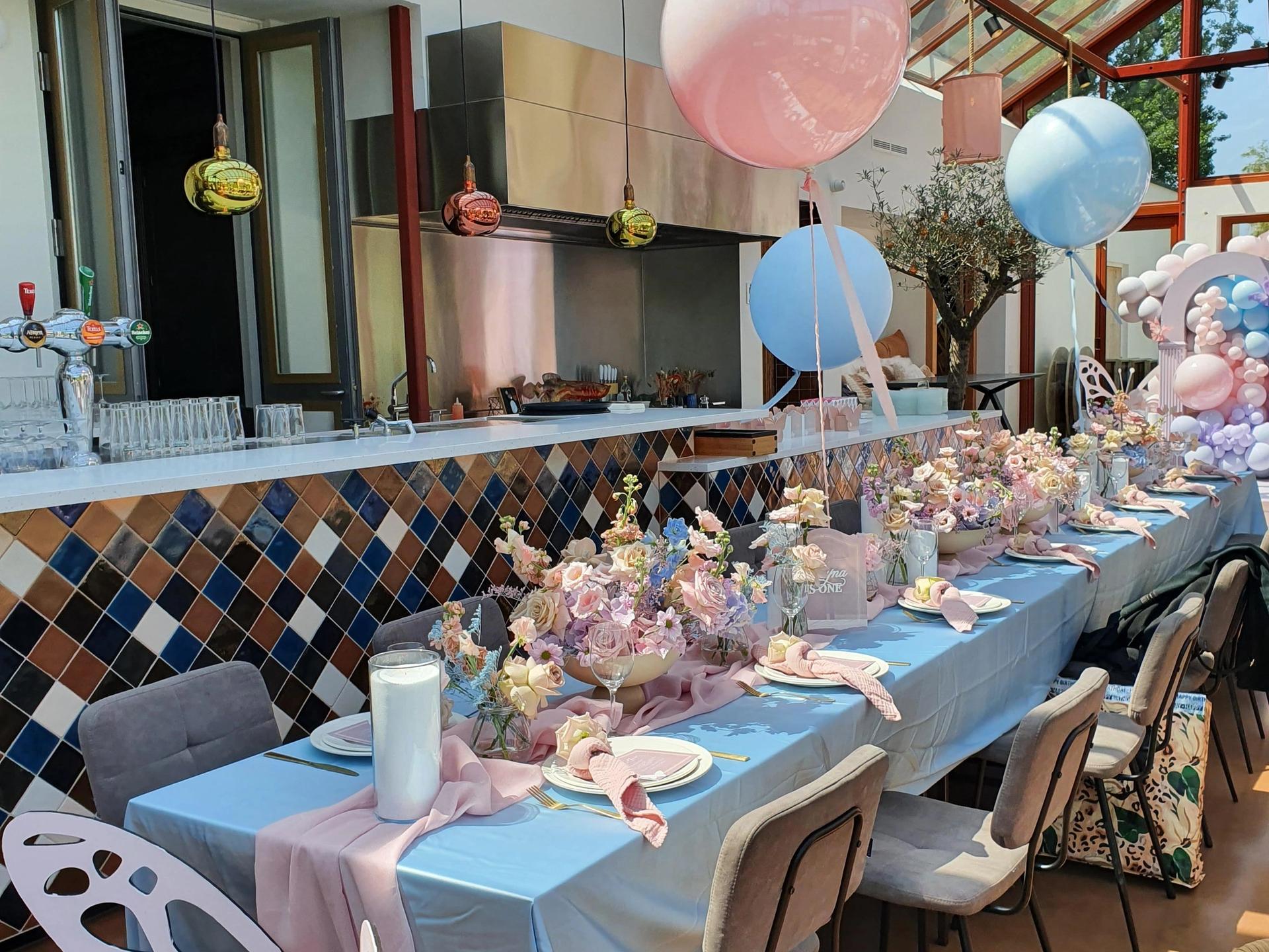 Babyshower in restaurant met roze en blauwe aankleding en versiering op gedekte lange tafels.