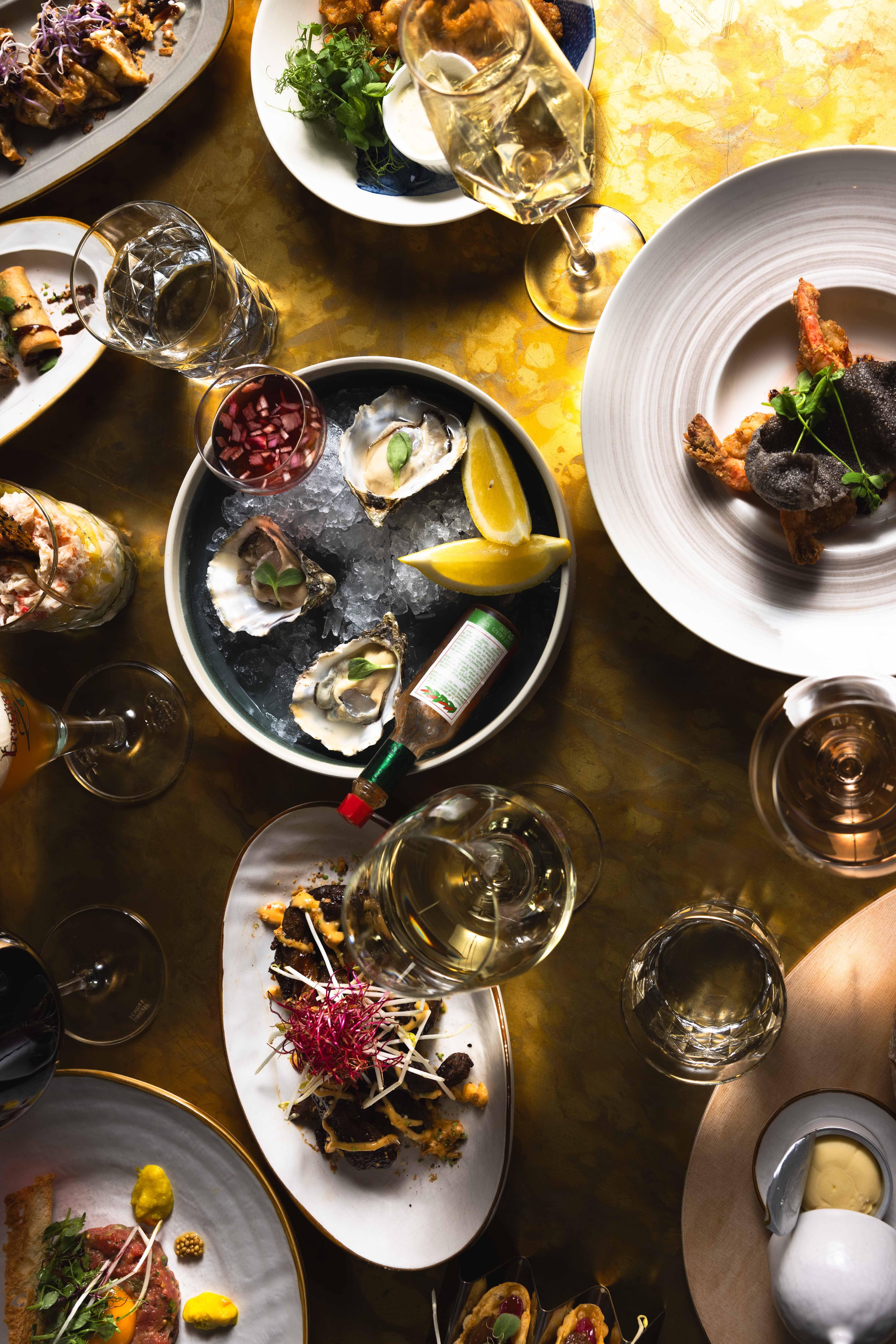 Tafel vol gerechten om te delen, met oesters op ijs, citroen en witte wijn bij La Cocotte