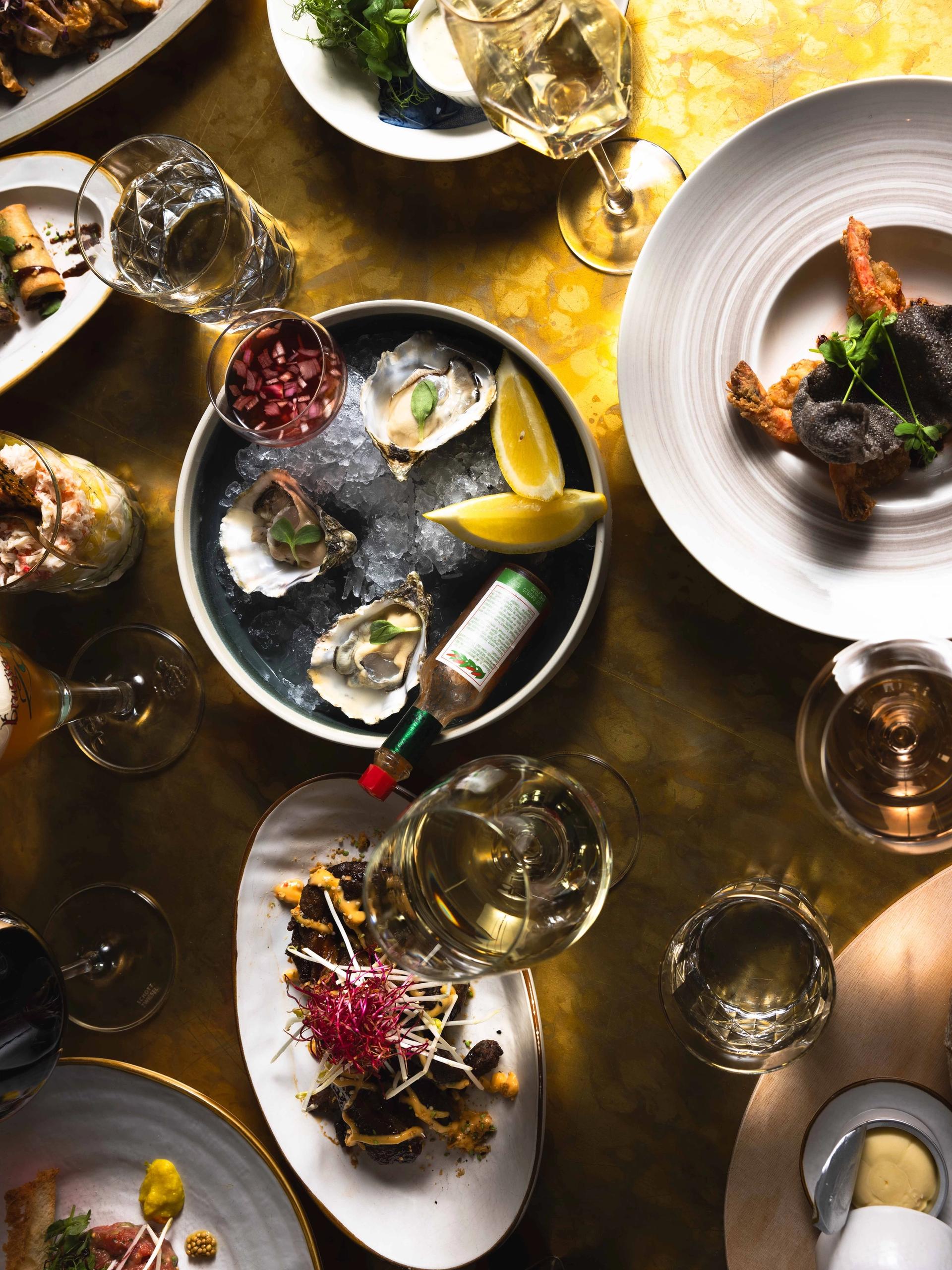Tafel vol gerechten om te delen, met oesters op ijs, citroen en witte wijn bij La Cocotte