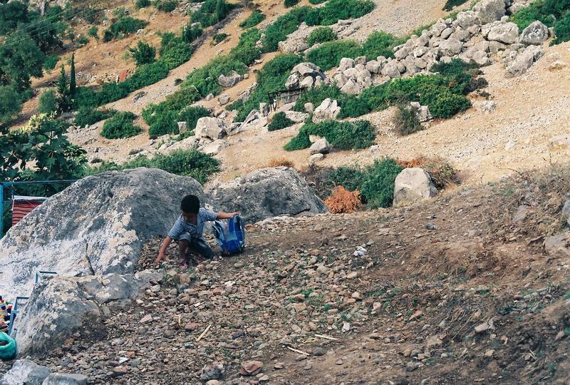 a boy on a hill fills a bag with rocks