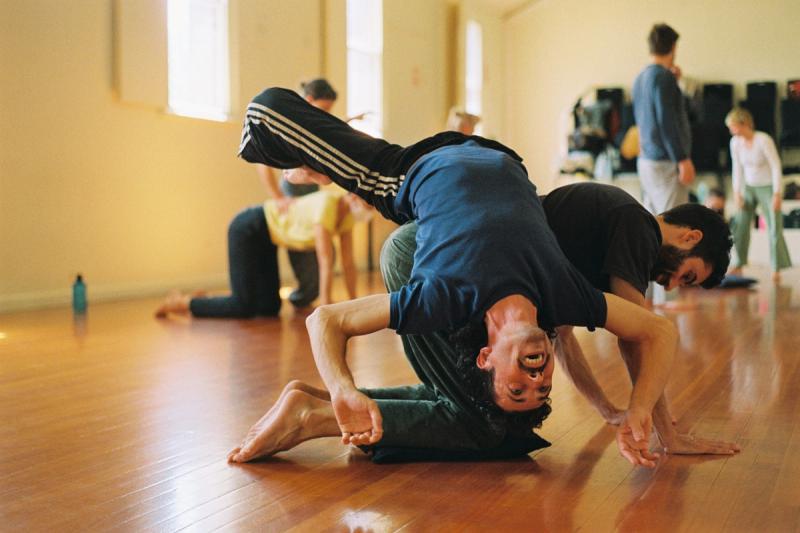 two men practice a contact improvisation balance in a sunny dance studio