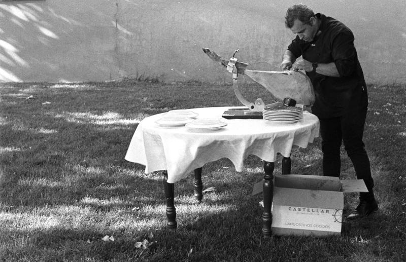 a man cuts a large leg of ham at a table in the garden