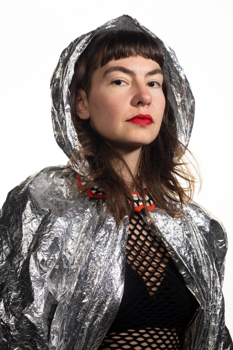 a portrait of a woman wearing a red lipstick and necklace, a silver hood and a black fishnet top photographed by Lorien Shannon 