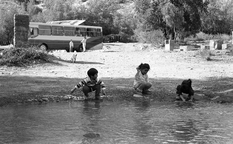 a black and white photo of children playing by a stream