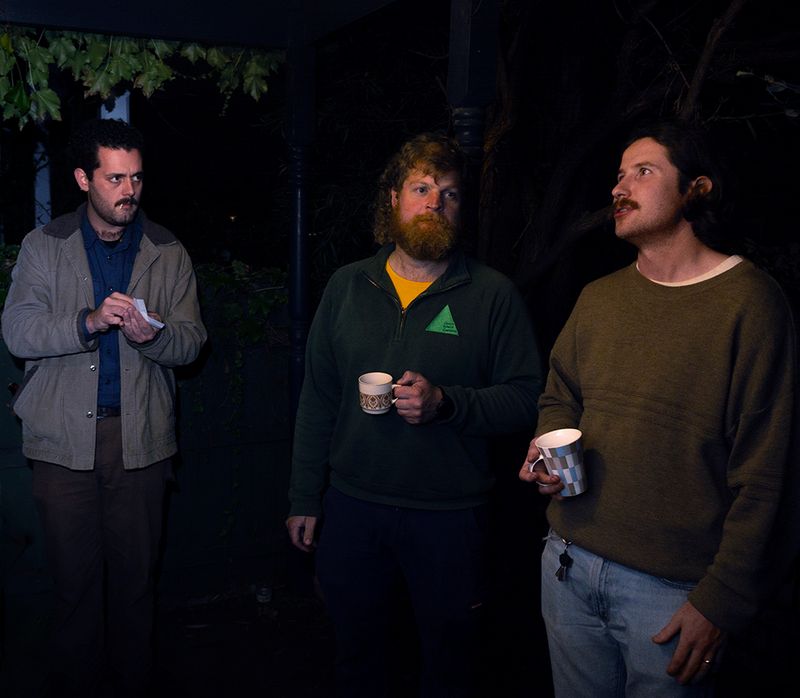 three men standing outside at night drinking tea