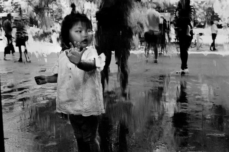 a black and white photo of a young child touching a window with water on it at the NGV