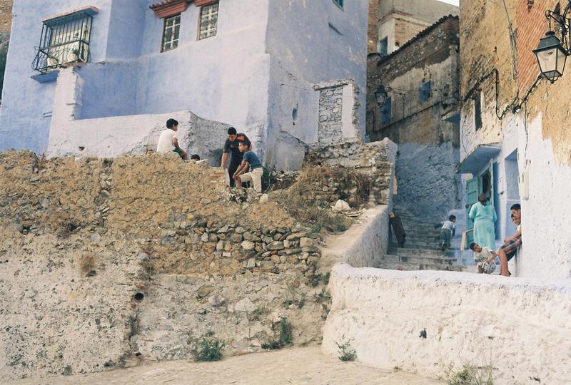 chafchaouen morocco, children play on stairs in front of old blue buildings 