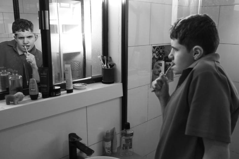 black and white photo of a boy brushing his teeth in the mirror