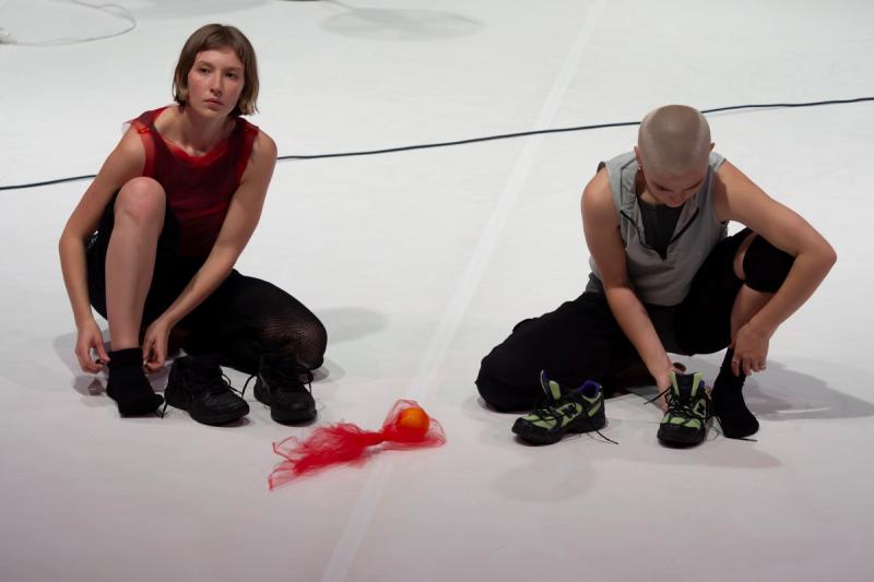 two dancers sit on a white stage putting runners on