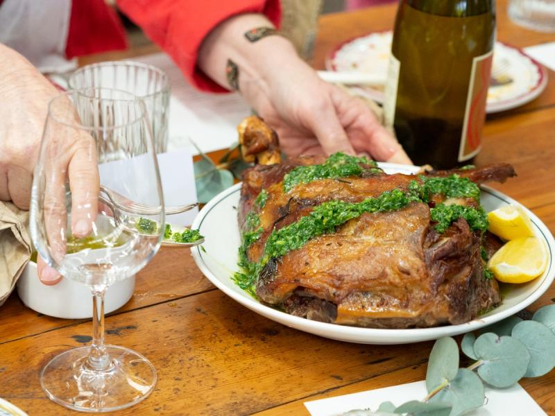 a hand reaching for a plate of roast lamb on a table