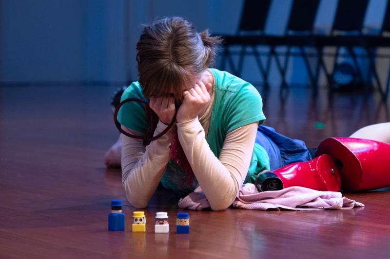 a dancer lies on the floor surrounded by toys with their face in their hands
