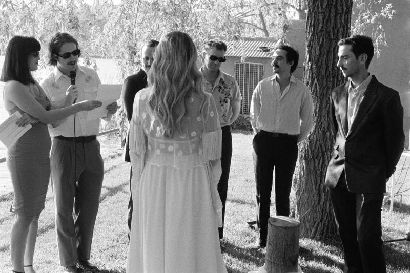 a bride and groom stand before the celebrants under a tree on a lake