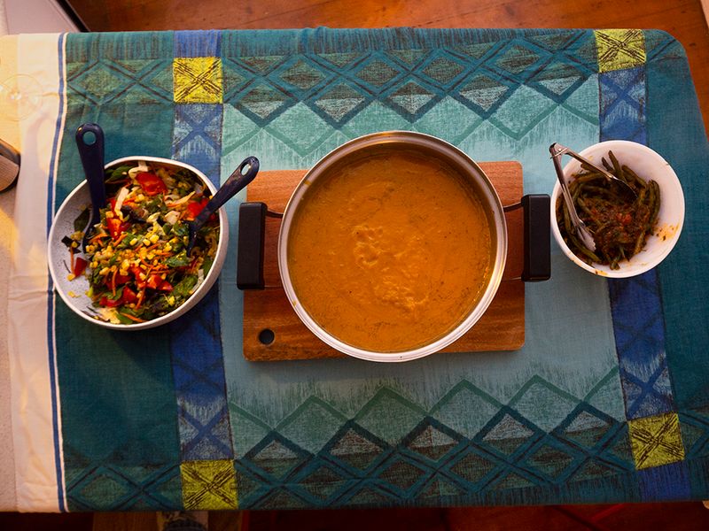 a Birdseye view of a kitchen bench with a table cloth, a pot of soup and two salads