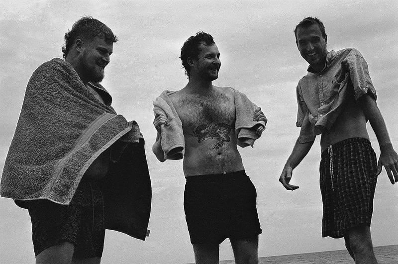 a black and white photo of friends Lloyd O' Hanlon, Carlo Manwell and Nial Hosken laughing at Point Addis beach