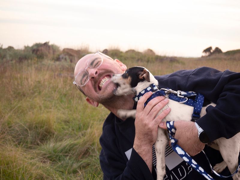 a man outside holding a puppy who is biting his chin 