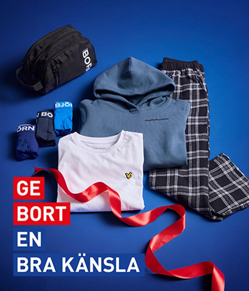 A gift set of a blue hoodie, white t-shirt, plaid pants, underwear, and a black toiletry bag, arranged on a blue background with a red ribbon.