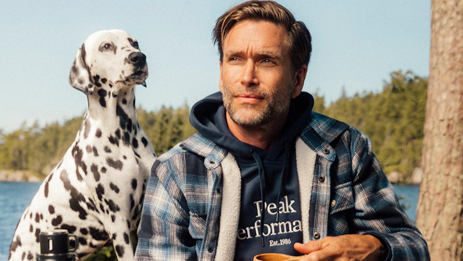 a man in a new jacket is sitting next to a dalmatian dog .