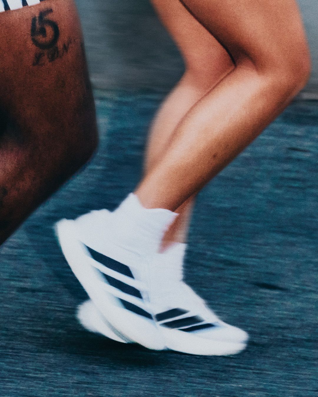 Two runners in motion blur, one with a "5 ICON" tattoo, the other wearing white Adidas sneakers.
